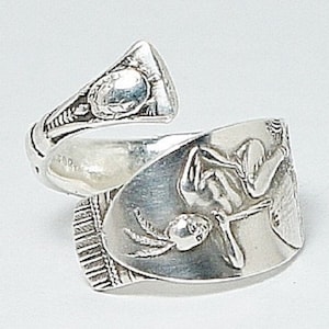 May include: A silver spoon ring with a detailed design of a woman holding a globe. The ring is made from a repurposed spoon and has a unique, handcrafted look.