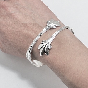 May include: A silver bangle bracelet with a decorative design on the ends. The bracelet is wrapped around a wrist.