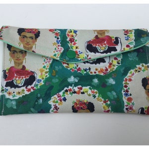 May include: A green and white fabric clutch with a floral pattern and a portrait of Frida Kahlo. The clutch has a green button closure.