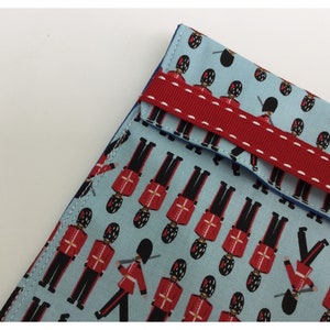 May include: A blue fabric pouch with a red ribbon closure. The pouch is decorated with a repeating pattern of red and blue toy soldiers.