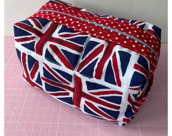 Puede incluir: Una bolsa con cremallera de color rojo, blanco y azul con estampado de Union Jack sobre un fondo blanco y una cremallera azul.