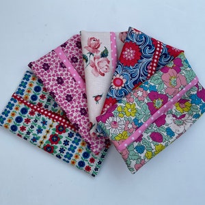 May include: Five fabric pouches with floral patterns and pink and red trim. The pouches are arranged in a fan shape.
