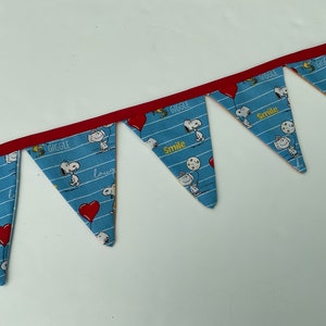 May include: A blue and white fabric banner with red trim. The banner has a repeating pattern of Snoopy characters and the words "Giggle" and "Smile".