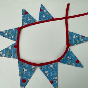 May include: A blue and red fabric banner with a white background. The banner has a red trim and features a repeating pattern of Snoopy characters and the words "Smile", "Giggle", "Love", and "Laugh".