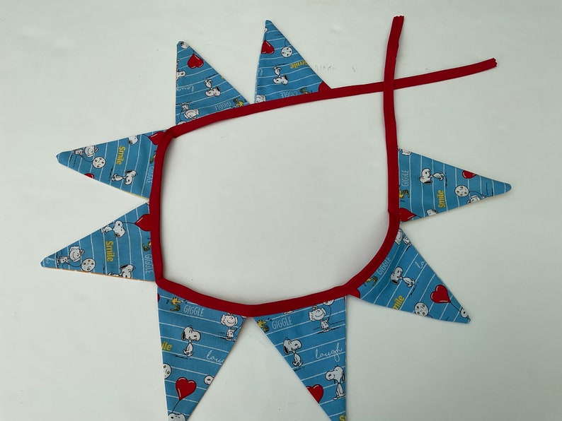 May include: A blue and red fabric banner with a white background. The banner has a red trim and features a repeating pattern of Snoopy characters and the words "Smile", "Giggle", "Love", and "Laugh".