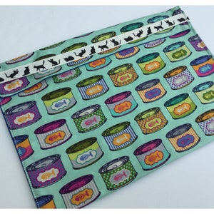 Peut inclure: Une pochette en tissu bleu sarcelle avec un ruban blanc et des silhouettes de chats noirs. La pochette est décorée d'un motif répété de boîtes de conserve pour chats colorées avec des arêtes de poisson.