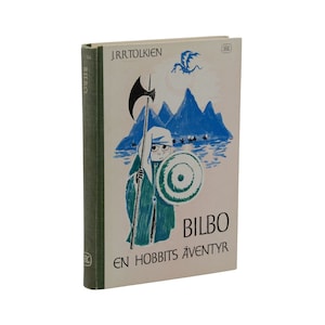 May include: A vintage hardcover book titled "Bilbo En Hobbits Äventyr" by J.R.R. Tolkien. The cover features a teal illustration of a figure with a spear and shield, mountains, and a dragon. The spine is green.
