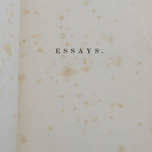 May include: A close-up of a page from a book with the word "ESSAYS" printed in black ink on a white background. The page is slightly yellowed and has several small brown spots.