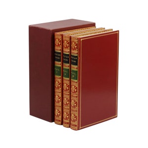 Peut inclure: Un ensemble de trois livres avec un coffret assorti. Les livres ont des couvertures rouges avec des bordures dorées et des dos avec des lettres dorées et des motifs décoratifs. Le coffret et les couvertures sont de couleur rouge foncé.