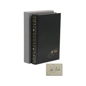 May include: A black leather-bound book with gold lettering titled "The Element" by John Grisham. The book is in a gray slipcase. The book is signed by the author.