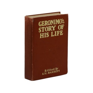 Op de afbeelding: Een bruin boek met de titel "Geronimo's Story of His Life" in gouden letters. Het boek is bewerkt door S.M. Barrett.