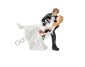 May include: A white wedding cake topper featuring a bride and groom in a romantic pose. The groom is holding the bride in his arms, and they are both smiling. The bride is wearing a white dress and a bouquet of red flowers. The groom is wearing a black suit and a white shirt.