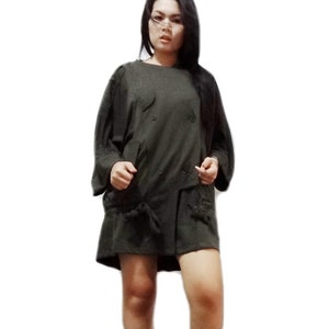 May include: A dark olive green dress with long sleeves and a double-breasted front. The dress features decorative buttons, pockets, and a skirt with a tied detail. The model is wearing the dress.