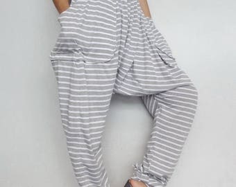 May include: Grey and white striped harem trousers with large pockets. The trousers are worn with a patterned top and grey sandals with wooden soles. The outfit is casual and comfortable.