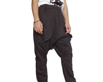 May include: Dark gray harem pants with a relaxed fit. The pants feature a drop crotch design, pockets, and visible stitching. The model is wearing a white t-shirt with a black graphic.