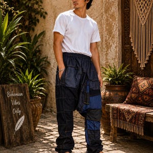 May include: A plain white short-sleeved t-shirt paired with loose-fitting, drop-crotch denim pants. The pants feature a patchwork design composed of various shades of blue and dark indigo denim fabric, an elastic waistband, and side pockets.