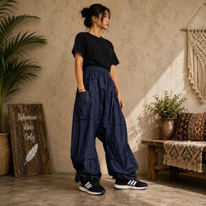 May include: A black short-sleeved t-shirt and loose-fitting dark blue denim pants with a dropped crotch, side pockets, and gathered ankles. The pants feature visible horizontal seam detailing across the legs and are paired with black and white sneakers.