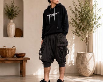 May include: A black hooded sweatshirt with white text reading WATERKANT KAFFEE on the chest, paired with dark charcoal gray drop-crotch cargo pants featuring side drawstrings and black athletic sneakers with white stripes on the sides.