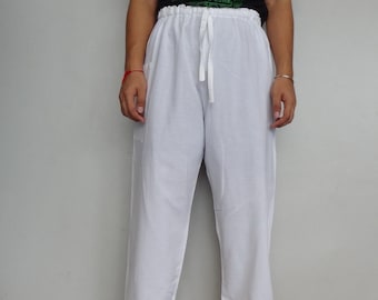 May include: White drawstring pants with a relaxed fit. The pants have a comfortable, loose design. The person in the image is also wearing a black t-shirt with green text and black sandals.