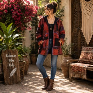 May include: A hooded jacket featuring a patchwork pattern in shades of red, black, and purple, worn over a black top with blue denim jeans and brown leather boots. The jacket has long sleeves, a front zip, and two side pockets.