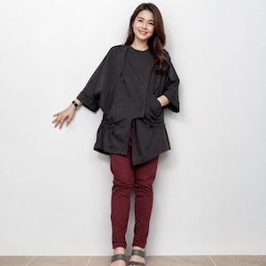 May include: A black double-breasted jacket with wide three-quarter length sleeves, shoulder epaulets, and a drawstring waist, paired with solid dark red trousers and grey open-toe sandals. The jacket features a front button closure.