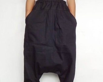 May include: Black harem trousers with an elasticated waistband and ankle cuffs. The trousers have large pockets and a loose, baggy fit. The person is wearing a white t-shirt and sandals.