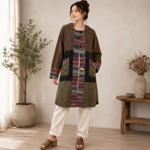 Puede incluir: Un abrigo con capucha y mangas largas que presenta un diseño de patchwork en tonos marrón, verde oliva y negro. El panel frontal y los puños están acentuados con un vibrante patrón tejido multicolor. El abrigo incluye dos bolsillos delanteros y cierre de botones.