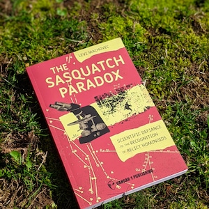 Op de afbeelding: Een rood boek met de titel "The Sasquatch Paradox" van Levi Machovec. De omslag toont een diagram en de tekst "Scientific Defiance to the Recognition of Relict Hominoids." Uitgegeven door Hangar 1 Publishing.