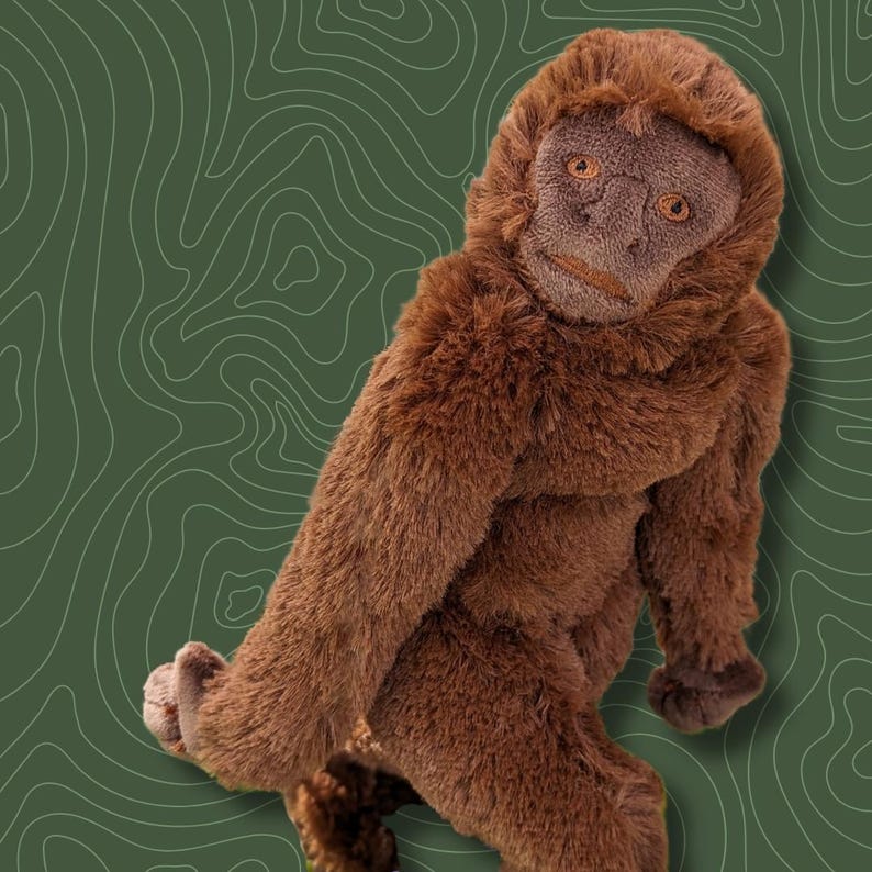 May include: A brown plush monkey toy with a realistic face and fur. The monkey is sitting with its legs crossed and its arms resting on its knees.