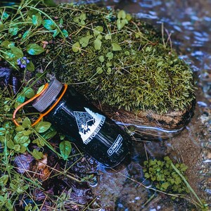 Może przedstawiać: Czarna butelka Nalgene z białym logo z napisem "The Forest Flew". Butelka leży w strumieniu wody i otoczona jest zielonym mchem.