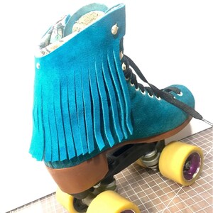 May include: Teal suede roller skate with fringe detail. The skate features black laces, gold eyelets, and yellow wheels with purple accents. The boot has a brown heel and a patterned interior.