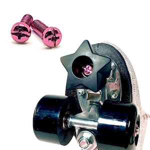 Puede incluir: Dos tornillos de metal rosa con un diseño en forma de estrella y un patín de ruedas negro con un tapón en forma de estrella. El tapón tiene una joya rosa en el centro.