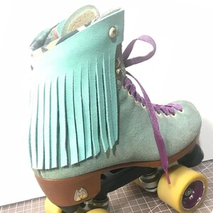 May include: A teal suede roller skate with purple laces and yellow wheels. The skate features a fringed teal leather accent and a brown heel. The wheels are yellow with purple accents. The skate has a classic design.