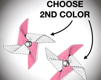 Puede incluir: Dos molinetes de fieltro rosa con aspas de fieltro blanco. Los molinetes tienen un clavo de metal plateado en el centro. El texto "CHOOSE 2ND COLOR" está escrito encima de los molinetes.