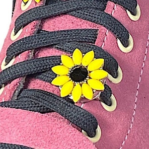 Puede incluir: Zapatillas de skate de gamuza rosa con cordones negros y abalorios de zapatos de girasol amarillo.