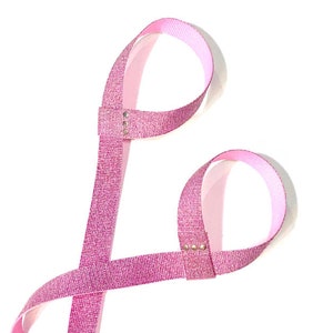 Puede incluir: Correa de yoga de color rosa con purpurina y dos lazos. La correa está hecha de un material suave y flexible y tiene un acabado brillante.