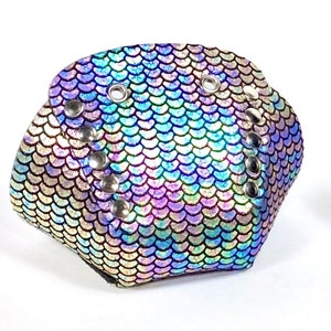 Puede incluir: Un par de cubrecalzados iridiscentes azul, morado y verde con tachuelas plateadas. Los cubrecalzados tienen un patrón de escamas.