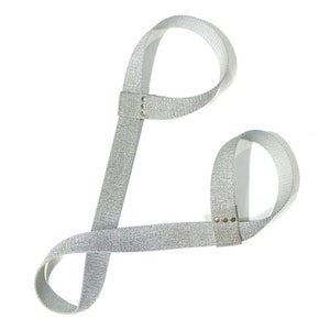 Puede incluir: Una pulsera de muñeca de brillo plateado con dos lazos y tachuelas plateadas.