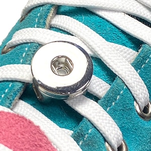 May include: Close-up of a turquoise and pink sneaker with white laces and a silver magnetic shoelace buckle.