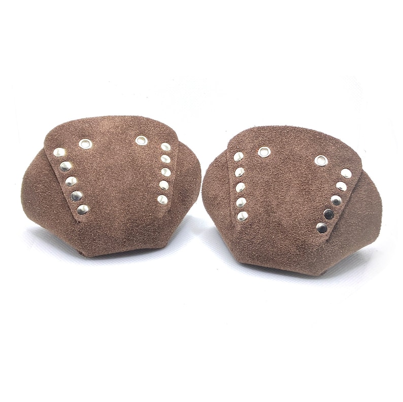 May include: Two brown suede leather knee pads with silver metal rivets. The knee pads are shaped like a rounded triangle.