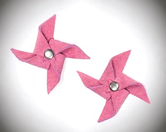Puede incluir: Dos molinetes de fieltro rosa con centros plateados. Los molinetes están sobre un fondo blanco.