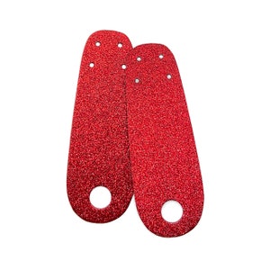 Op de afbeelding: Twee rode glitter schoen hielbeschermers met een gat in het midden.