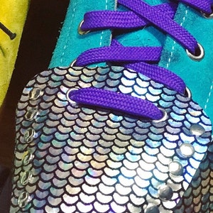K&ouml;nnte beinhalten: Ein Paar t&uuml;rkisblaue Sneaker mit lila Schn&uuml;rsenkeln und einer silbernen, irisierenden Pailletten-Zehenkappe. Die Zehenkappe hat ein gewelltes Design und ist mit silbernen Nieten verziert.