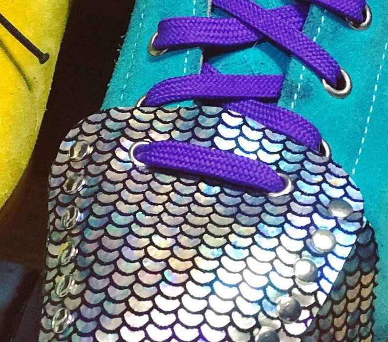 K&ouml;nnte beinhalten: Ein Paar t&uuml;rkisblaue Sneaker mit lila Schn&uuml;rsenkeln und einer silbernen, irisierenden Pailletten-Zehenkappe. Die Zehenkappe hat ein gewelltes Design und ist mit silbernen Nieten verziert.