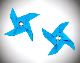 Puede incluir: Dos molinetes de fieltro azul con centros plateados. Los molinetes están sobre un fondo blanco.