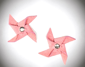 Puede incluir: Dos molinetes de fieltro rosa con centros de metal plateado. Los molinetes están sobre un fondo blanco.