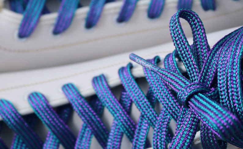 K&ouml;nnte beinhalten: Nahaufnahme eines Paares wei&szlig;er Sneaker mit t&uuml;rkisfarbenen und violetten Schn&uuml;rsenkeln. Die Schn&uuml;rsenkel sind in einem Kreuzmuster gebunden.