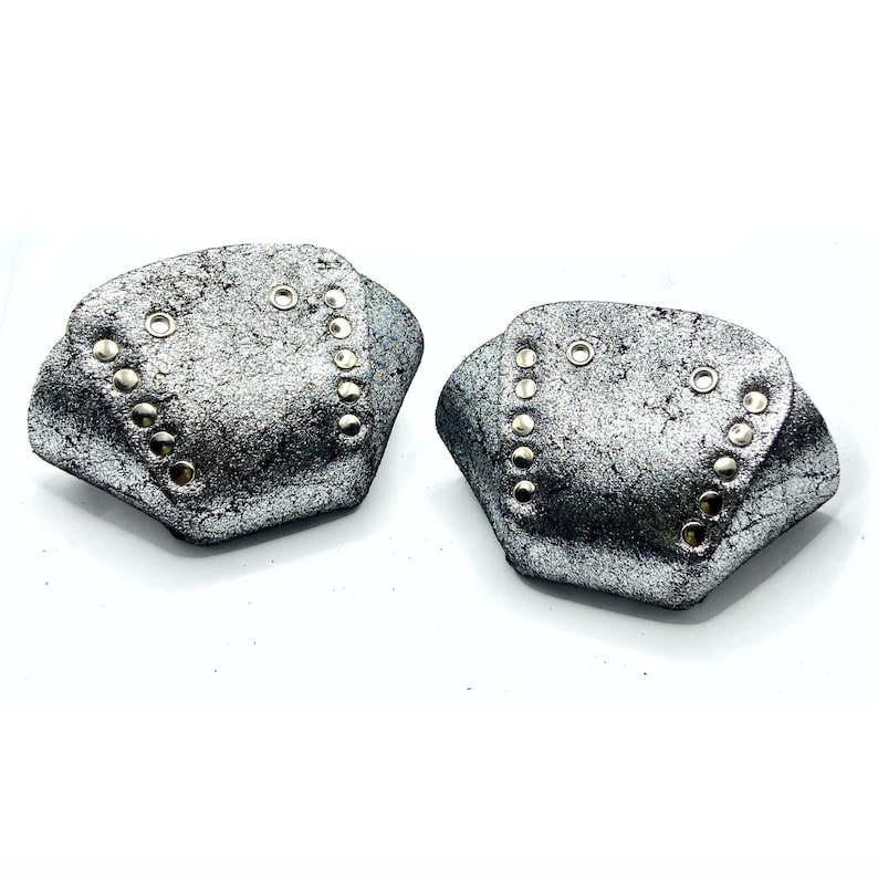 May include: Two silver leather shoe protectors with silver studs. The protectors are shaped like a diamond and have a textured surface.