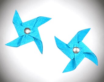 Puede incluir: Dos molinetes de fieltro azul con centros plateados. Los molinetes están sobre un fondo blanco.