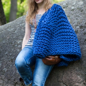 May include: A woman wearing a blue chunky knit cardigan with a brown leather bag. She is wearing a striped shirt and blue jeans.